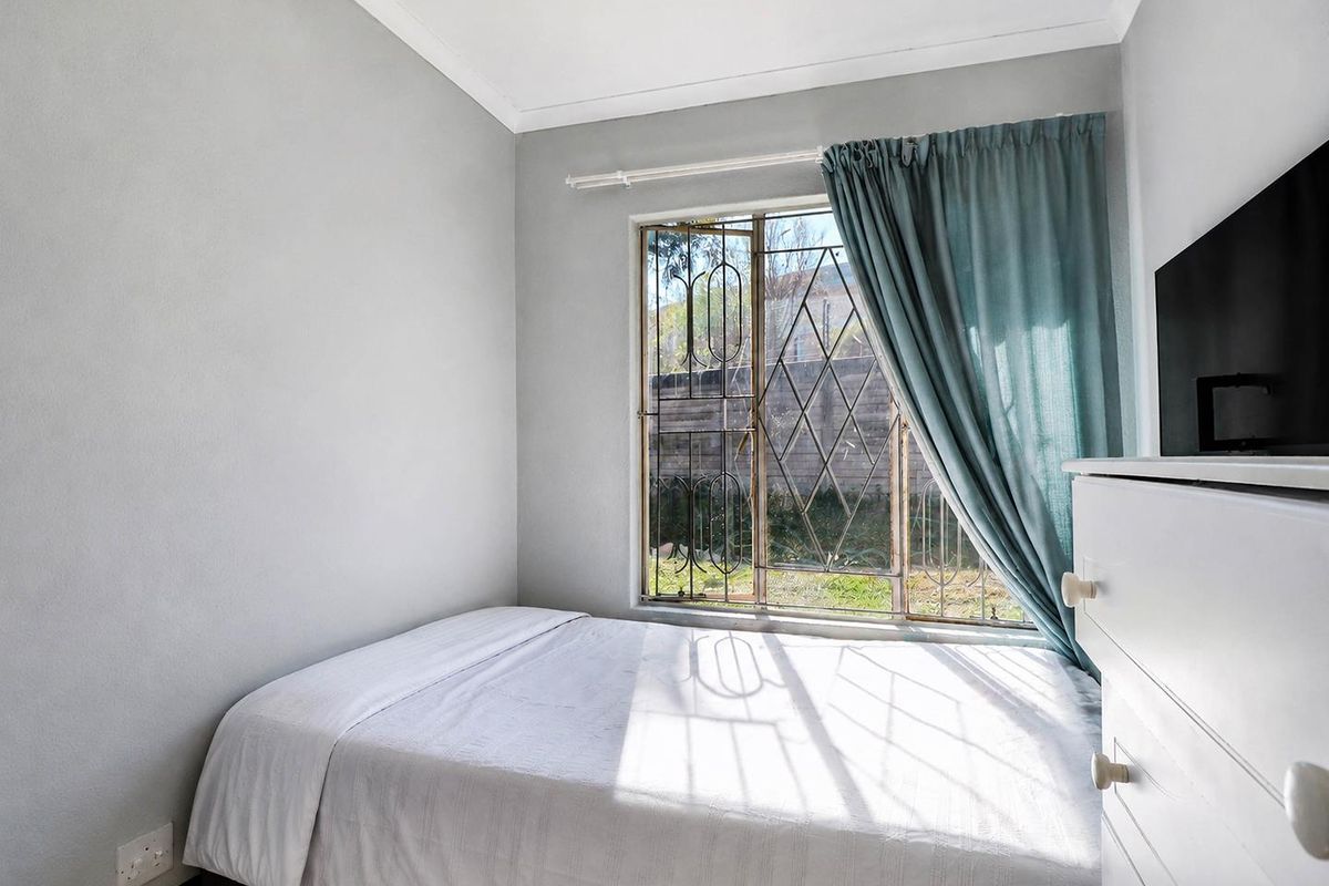 A compact bedroom featuring neutral wall finishes, a window with integrated security bars, and tiled flooring.