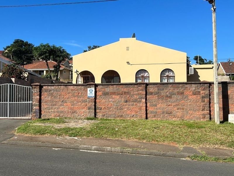 Front elevation of a residential property featuring a prominent brick boundary wall, secure metal gate, and arched window detailing.
