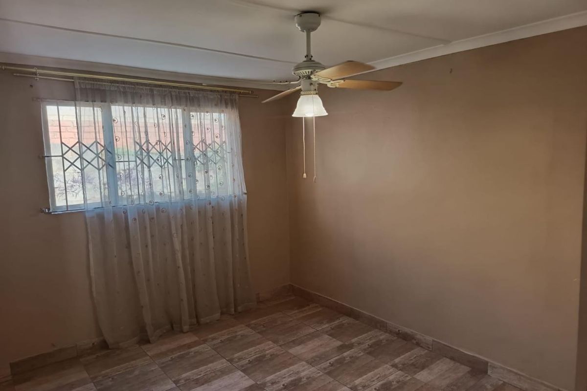 An empty bedroom featuring tiled flooring, a ceiling fan, and a window fitted with a security gate.