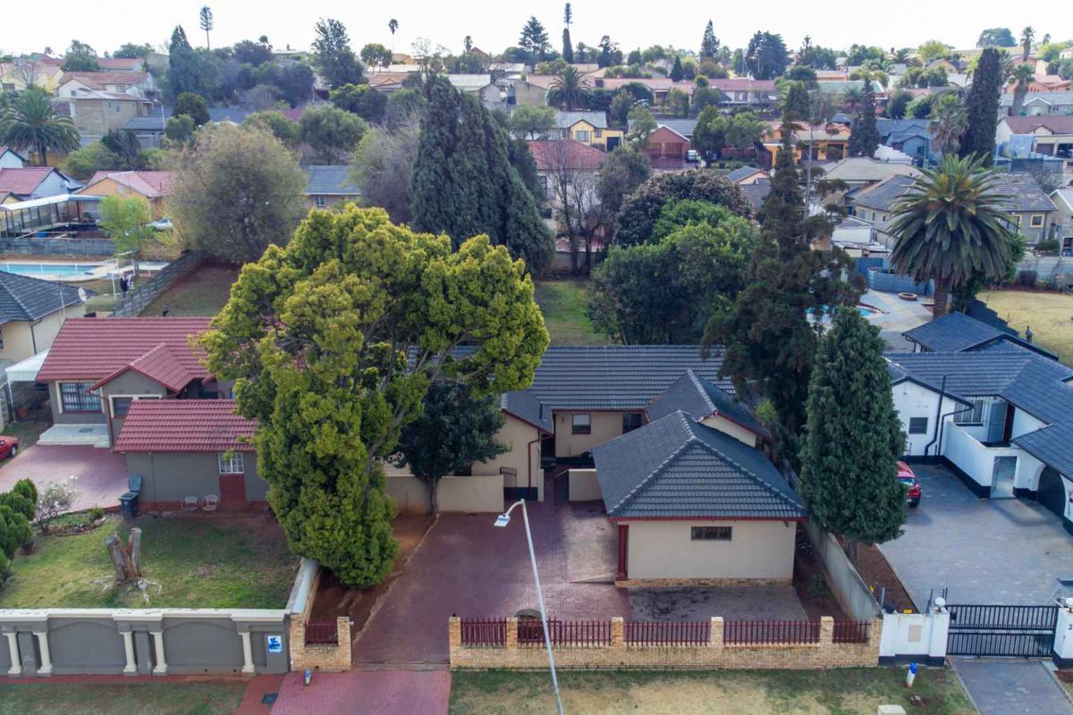 Aerial view of a residential property featuring a tiled roof house, paved driveway, and established garden within a suburban neighborhood.