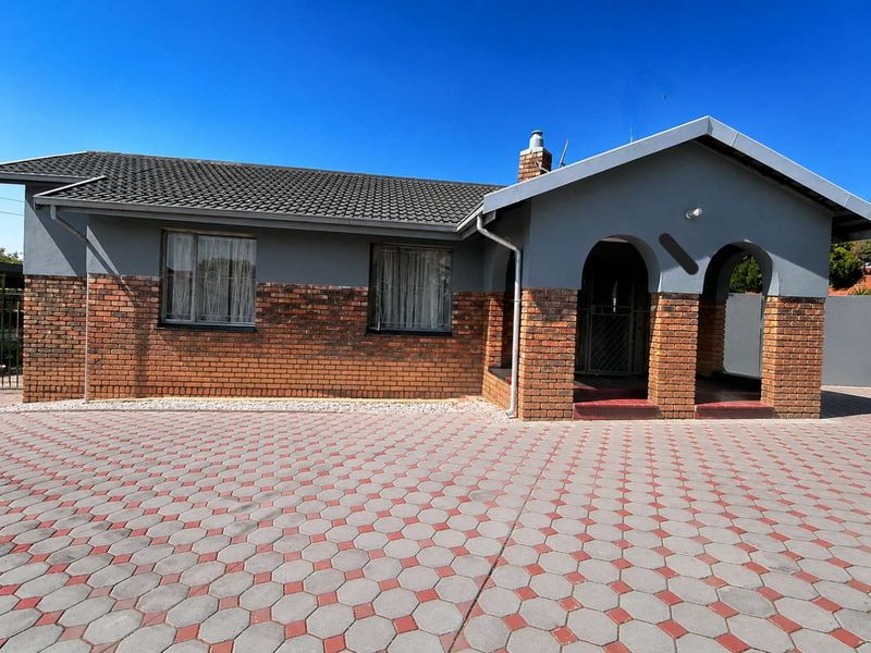 Front elevation of a well-maintained house featuring a brick and rendered facade, arched entrance porch, tiled roof, and a spacious paved driveway.
