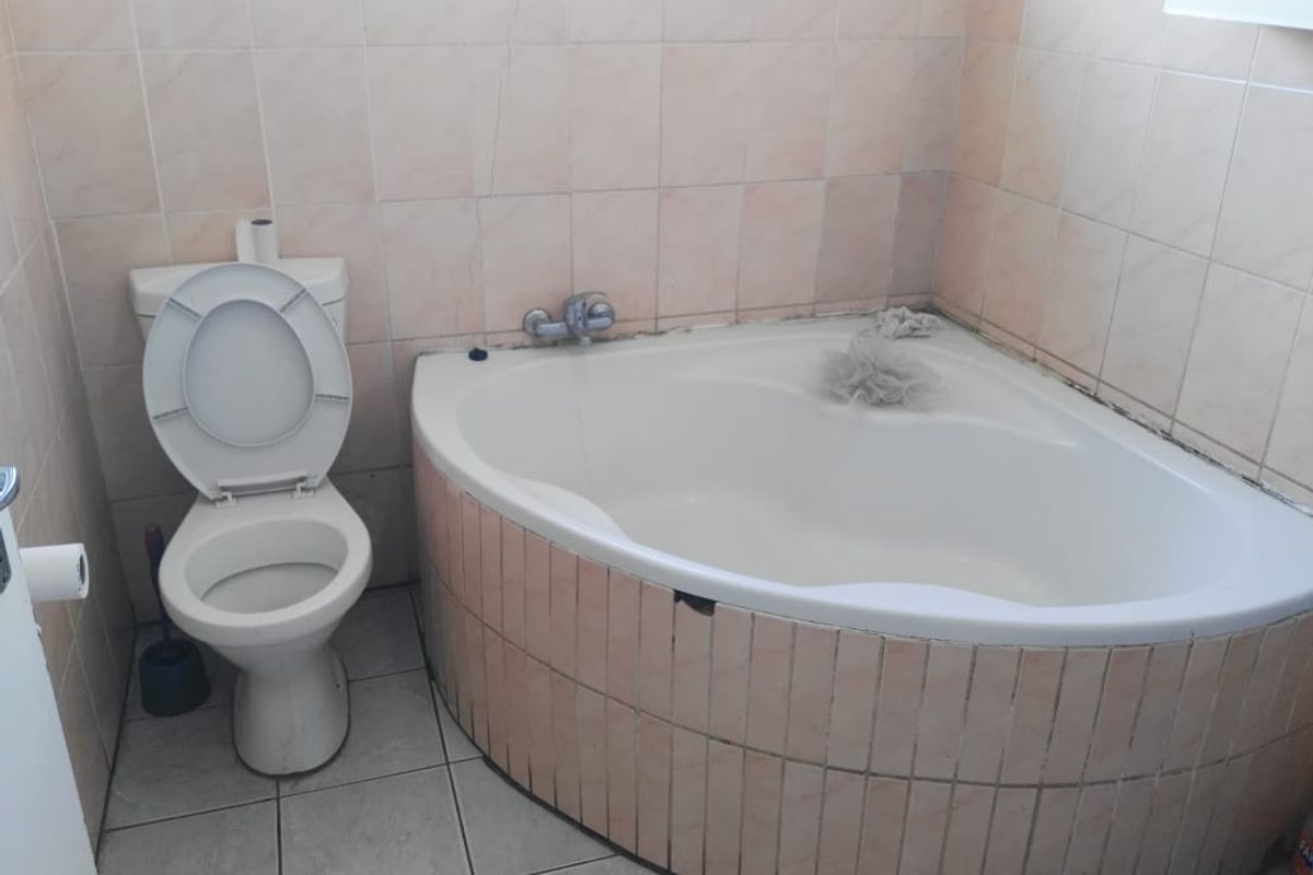 A dated bathroom featuring a corner bathtub with tiled apron and a standard toilet, requiring cosmetic updates to modernize the space.