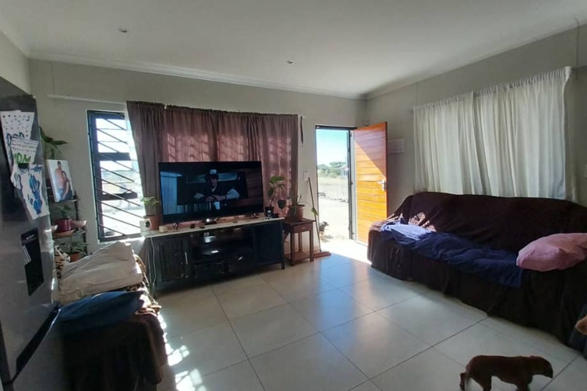 A living room area featuring tiled flooring, large windows with curtains, and direct access to the exterior through a wooden door.