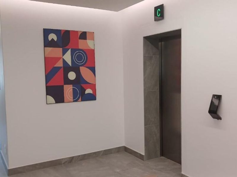 Modern office building hallway featuring a sleek elevator with stone surround, recessed ceiling lighting, and contemporary tiled flooring.