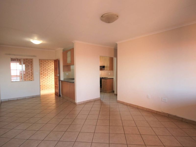 An open-plan living area featuring tiled flooring, neutral walls, and a view into the adjacent kitchen space.