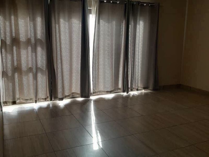 A spacious, empty living area featuring neutral tiled flooring, a coved ceiling, and a large sliding glass door with curtains.