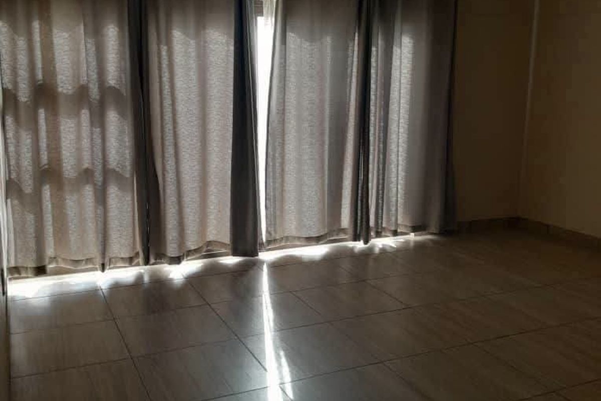 A spacious, empty living area featuring neutral tiled flooring, a coved ceiling, and a large sliding glass door with curtains.
