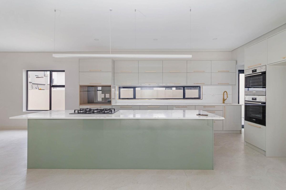 Modern kitchen featuring a large central island with a gas hob, sleek cabinetry, integrated double ovens, and high-quality stone countertops.