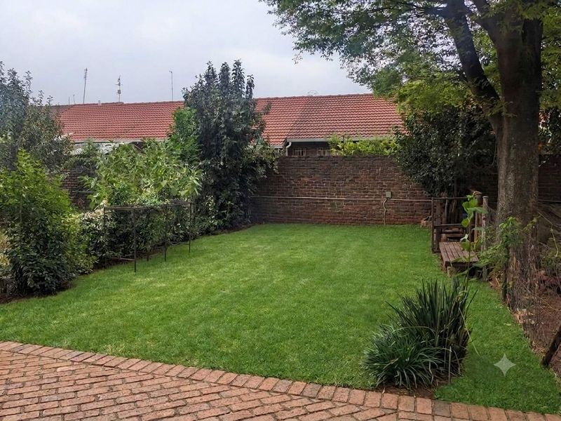 A well-maintained private garden featuring a lush green lawn, brick paving, and a secure brick boundary wall.