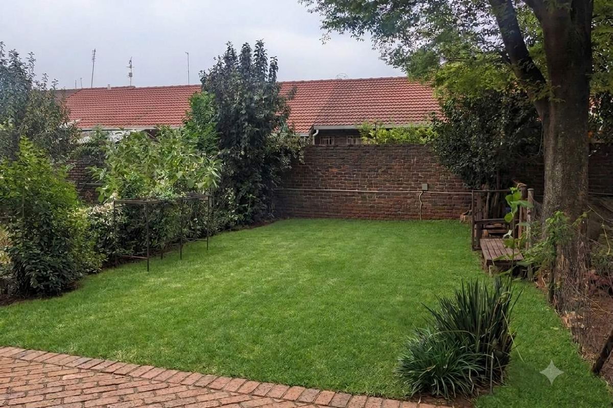 A well-maintained private garden featuring a lush green lawn, brick paving, and a secure brick boundary wall.