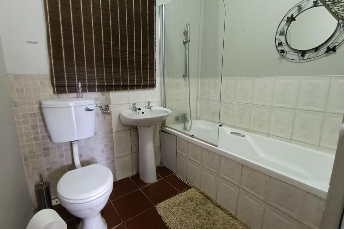A functional bathroom featuring a white pedestal basin, toilet, and a bathtub with a glass shower screen and wall-mounted shower head.