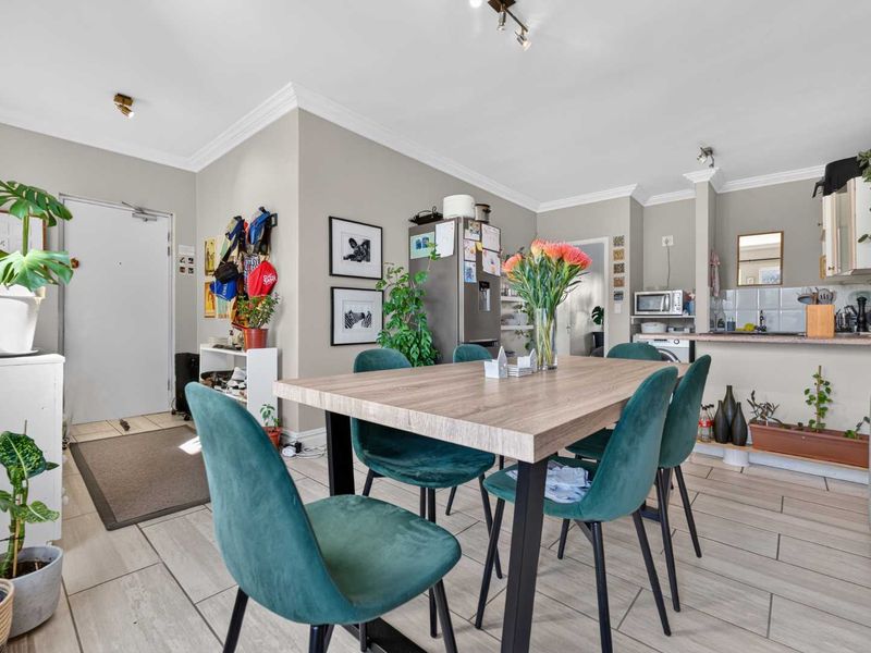Open-plan living and dining area featuring tiled flooring, neutral walls, and a functional kitchen with built-in cabinetry and a tiled backsplash.