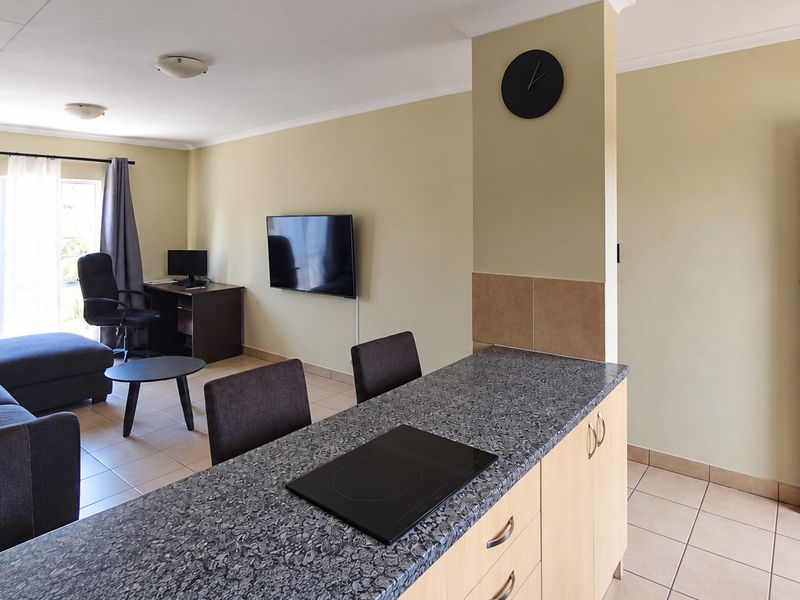 Open-plan living area featuring a kitchen with built-in cabinetry, electric cooktop, and tiled flooring, seamlessly flowing into the adjacent lounge space.
