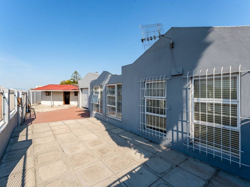 Rear exterior view of the property featuring a paved patio area, security bars on windows, and a boundary wall.