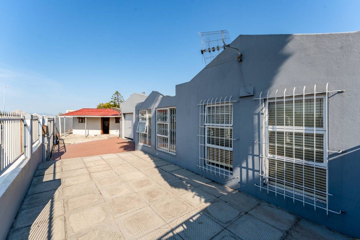 Rear exterior view of the property featuring a paved patio area, security bars on windows, and a boundary wall.