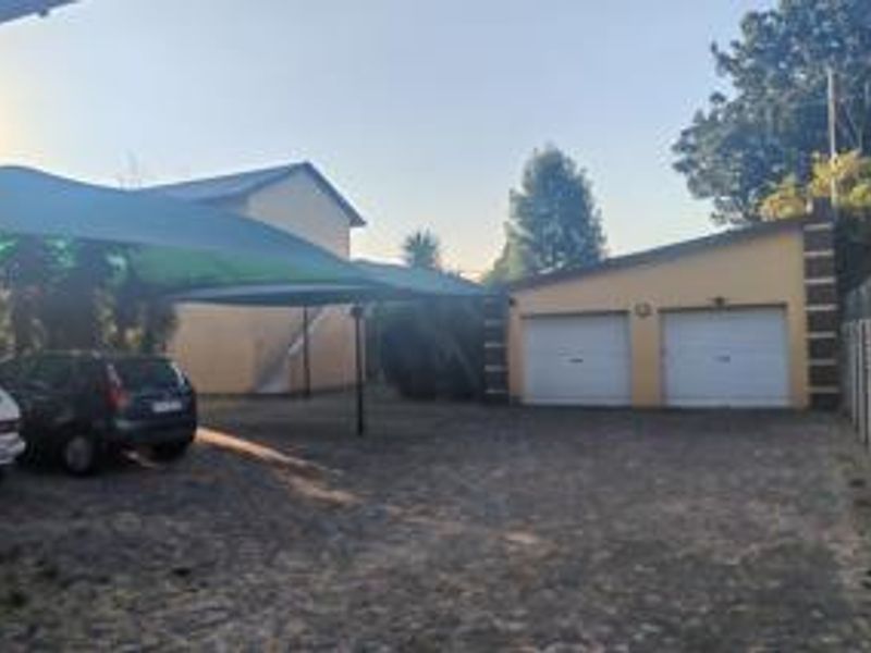 Exterior view of the property featuring a double garage, a paved driveway, and a shade cloth carport for additional vehicle parking.