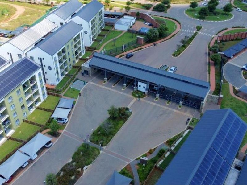 Aerial view of a modern apartment complex featuring solar panel installations, secure gated access, and dedicated carport parking areas.
