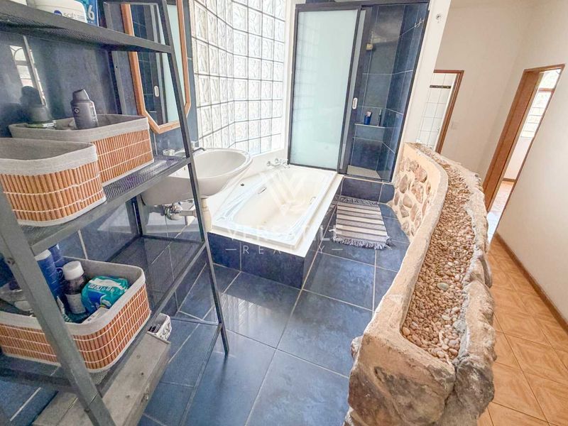 A bathroom featuring a built-in bathtub, glass shower enclosure, pedestal basin, and a unique stone-clad feature wall with glass block windows.