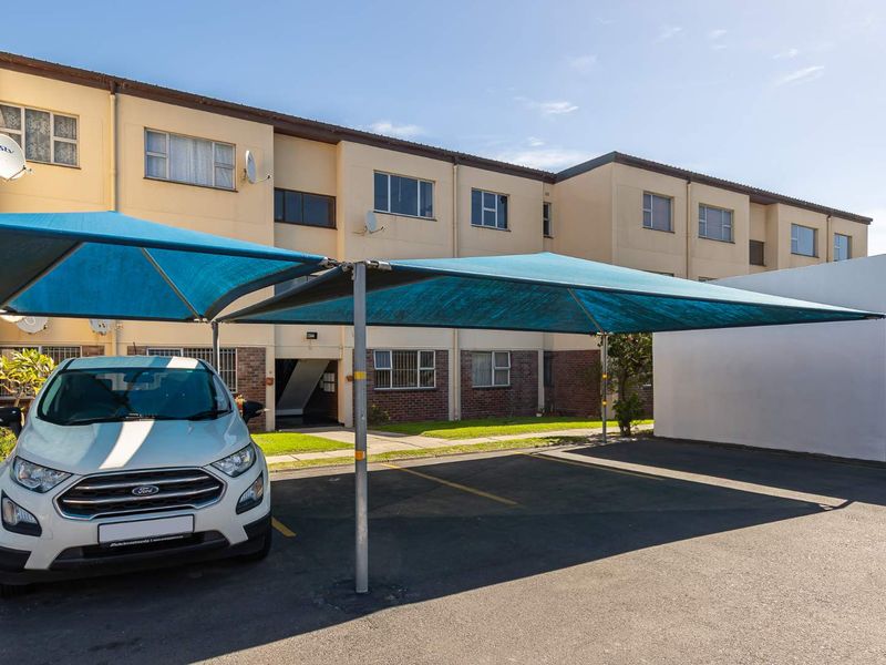Exterior view of an apartment complex featuring a paved parking area with blue shade cloth carports and brick and plaster facade.