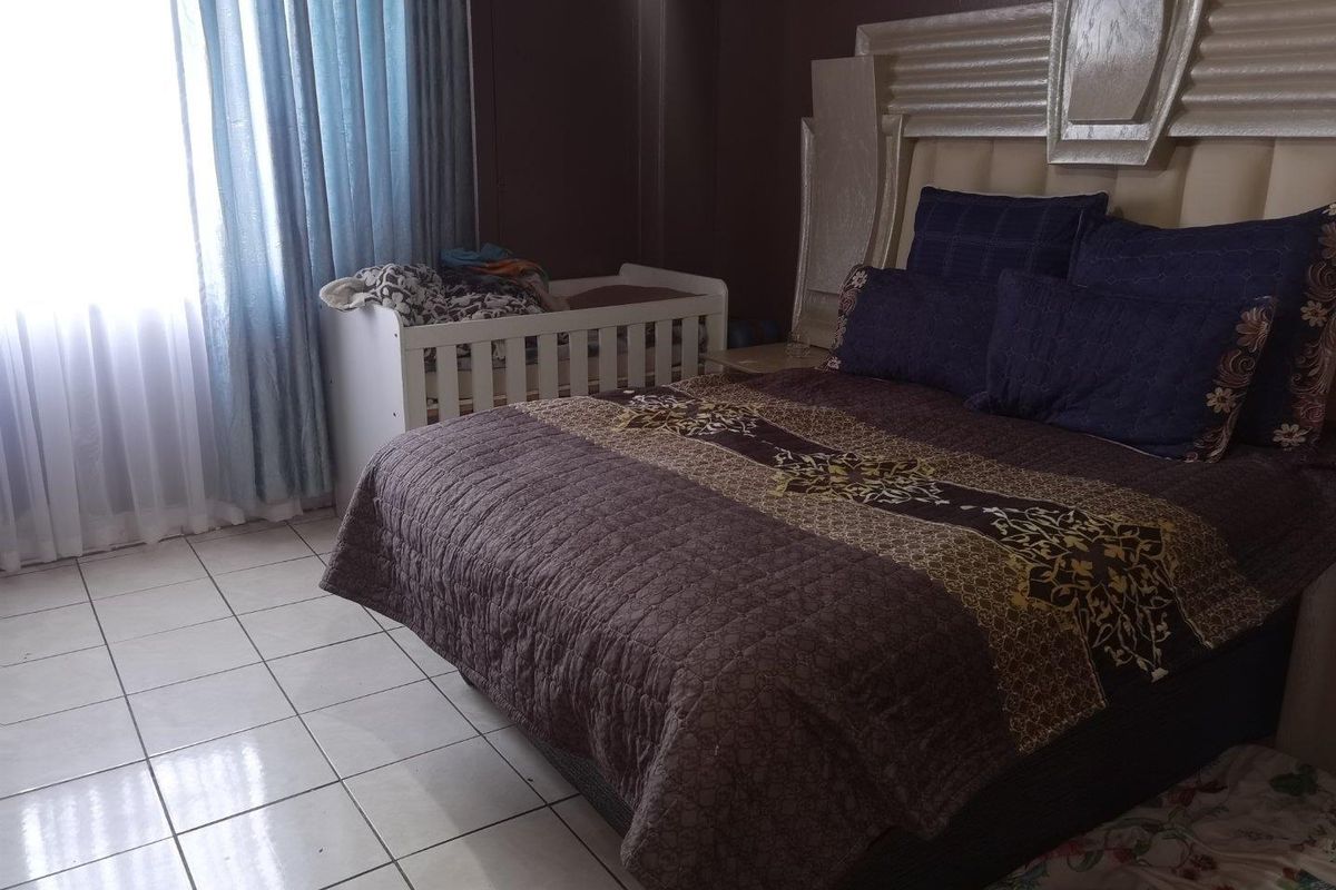 A bedroom featuring tiled flooring and a large window with curtains, providing a functional space for rest.