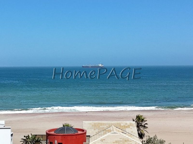 Elevated coastal view overlooking the beach and ocean, featuring a residential property with a tiled roof and garage.
