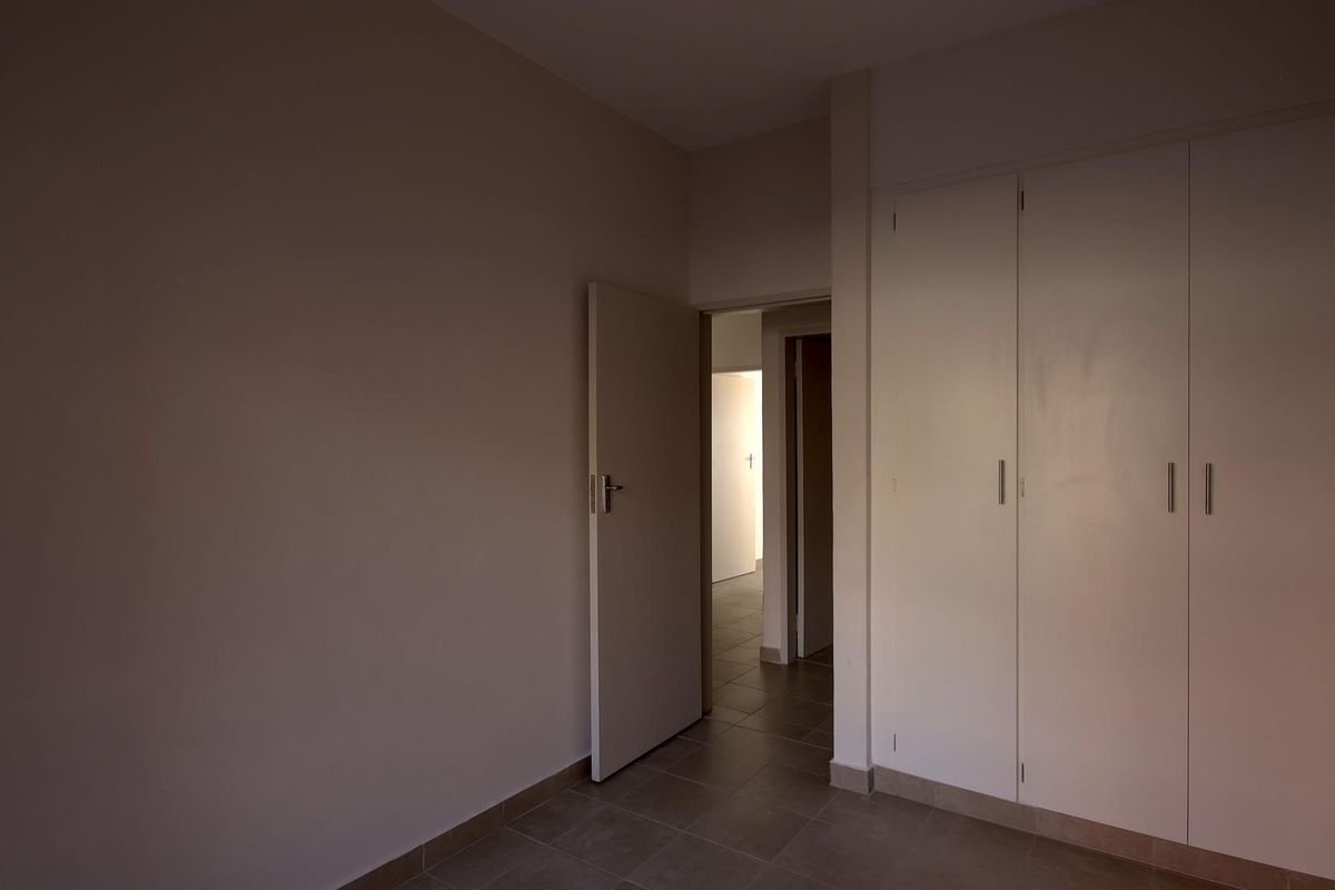 An empty bedroom featuring neutral walls, tiled flooring, and built-in cupboards, offering a clean and versatile space ready for personalization.