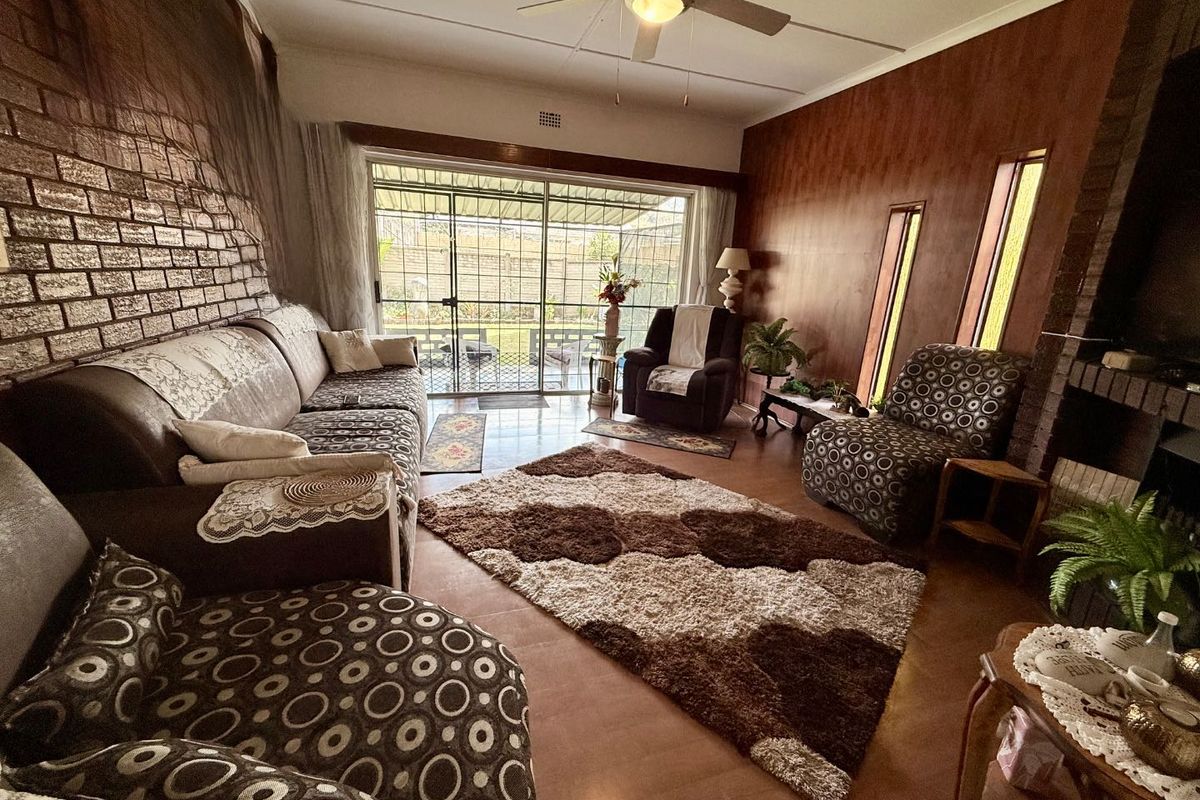 Spacious living room featuring a brick feature wall, wood-paneled walls, a ceiling fan, and large sliding glass doors leading to the outdoor area.