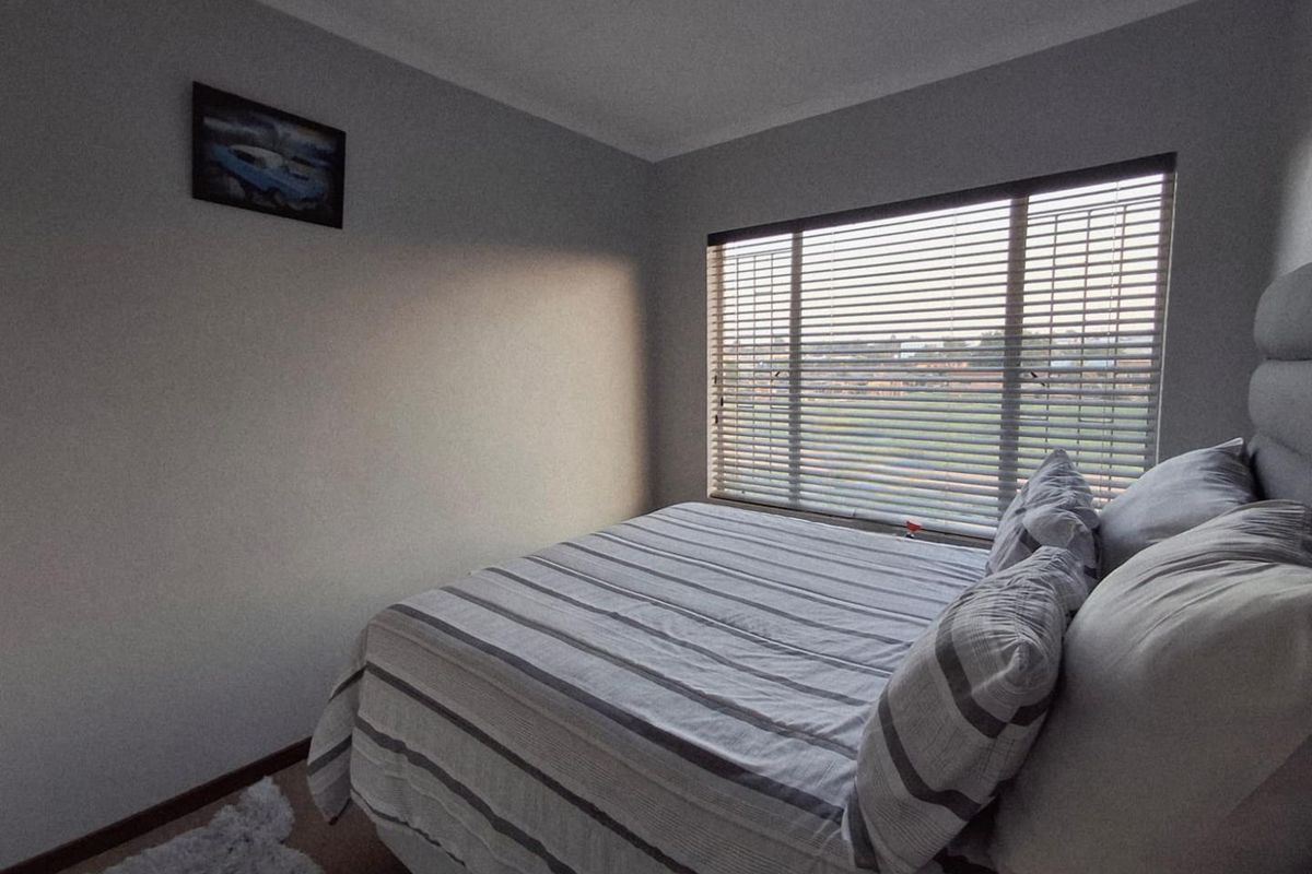 A functional bedroom featuring neutral walls, carpeted flooring, and venetian blinds on the window.