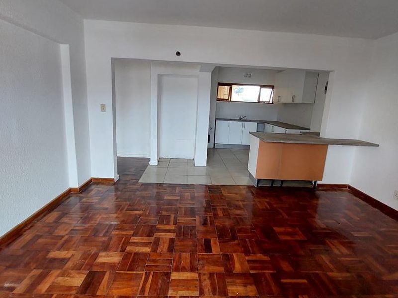 An open-plan living and kitchen area featuring traditional parquet flooring, a breakfast counter, and functional kitchen cabinetry in a dated but well-maintained condition.