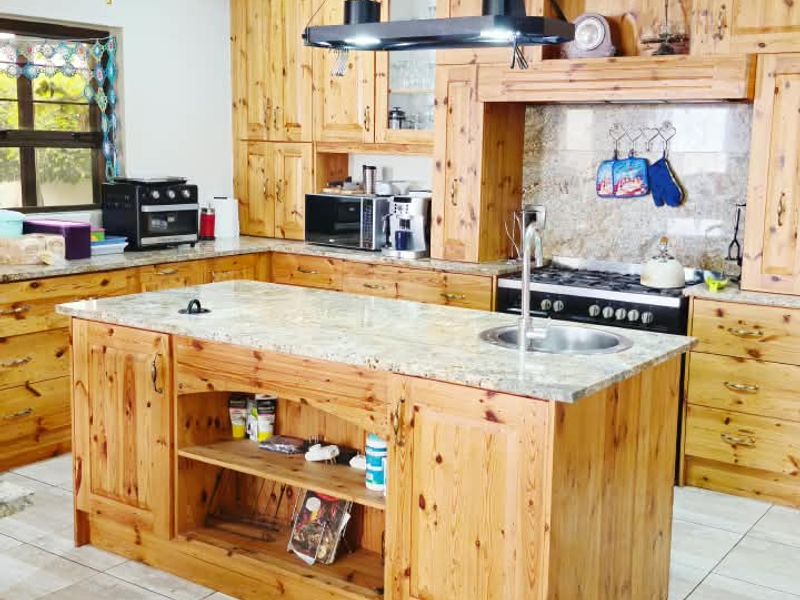 A spacious kitchen featuring extensive wooden cabinetry, a central island with a granite countertop, integrated sink, and a built-in stove with an extractor fan.
