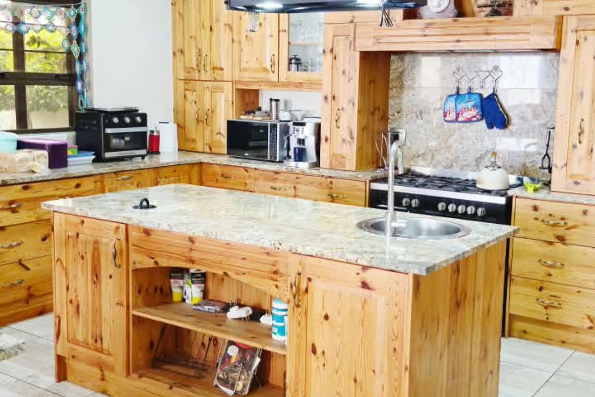 A spacious kitchen featuring extensive wooden cabinetry, a central island with a granite countertop, integrated sink, and a built-in stove with an extractor fan.