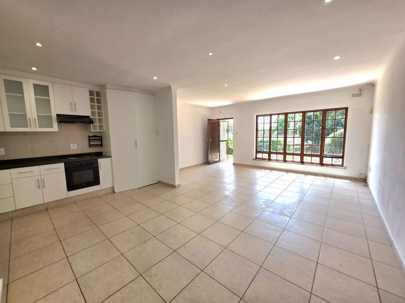 Spacious open-plan living area featuring a modern kitchen with built-in appliances, tiled flooring, and large windows providing ample natural light.