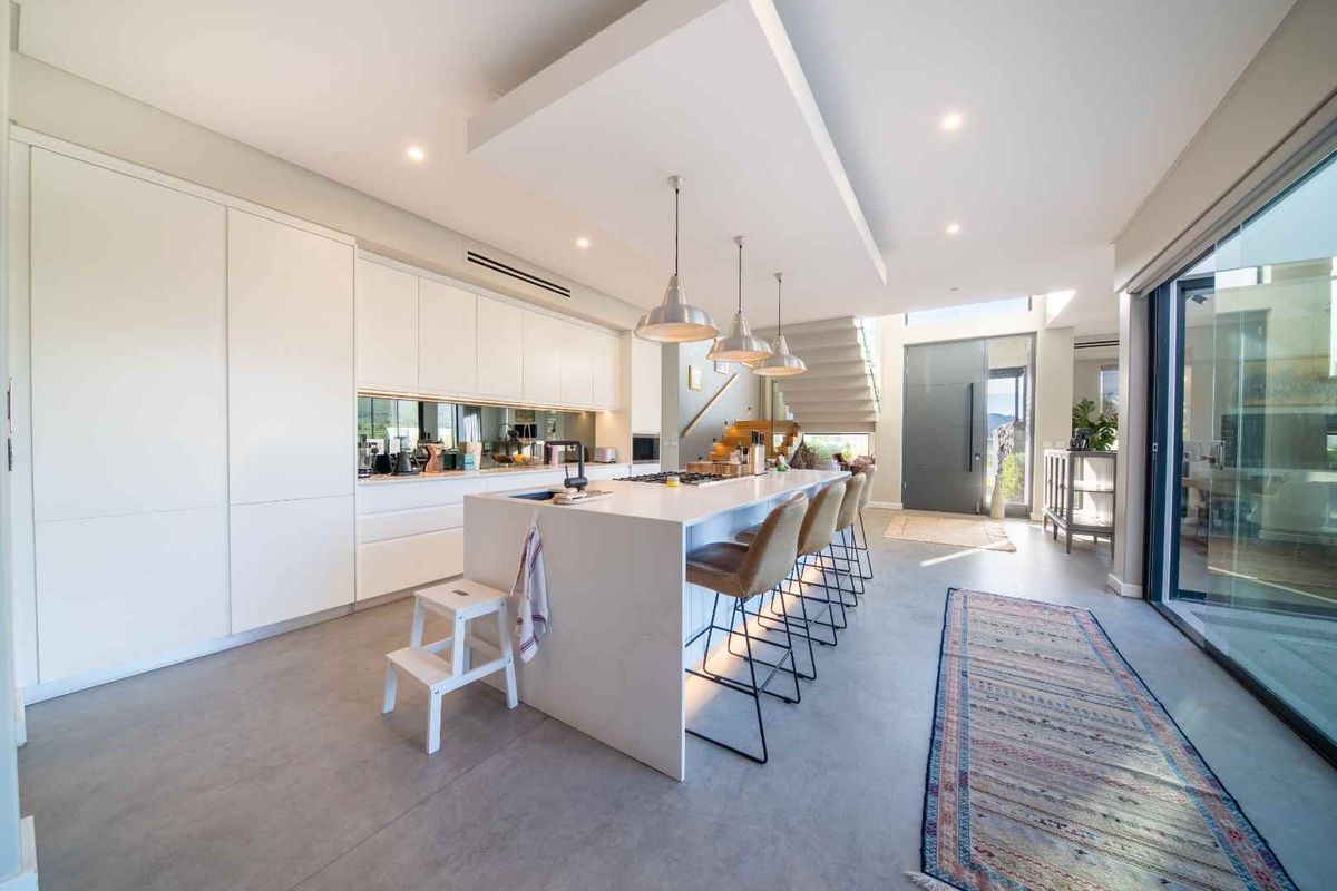 Modern open-plan kitchen featuring a large central island, sleek white cabinetry, mirrored splashback, and seamless access to outdoor areas through sliding glass doors.