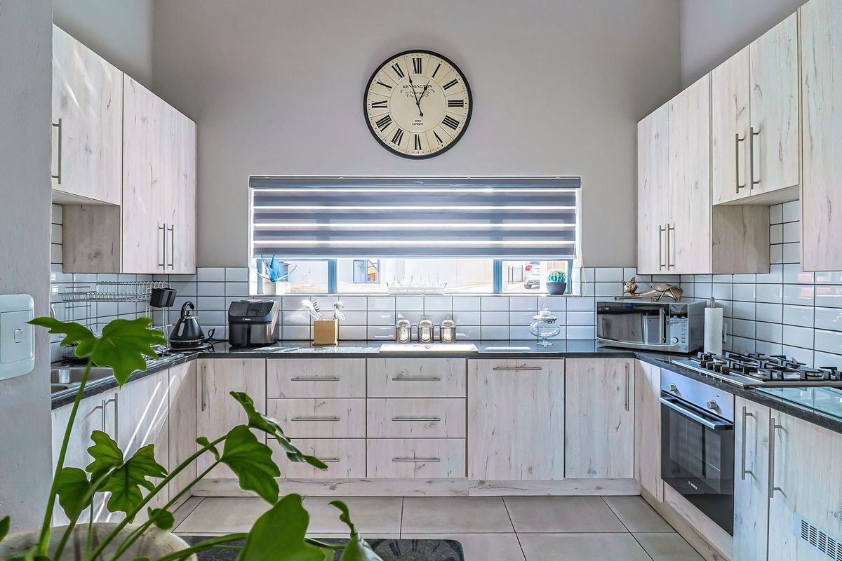 Modern kitchen featuring light wood-grain cabinetry, dark stone countertops, subway tile backsplash, and integrated stainless steel oven and gas hob.