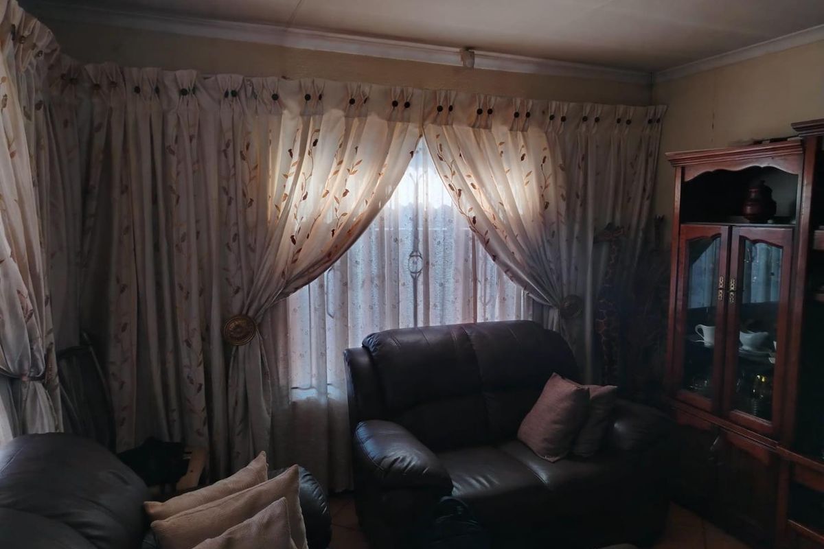 A living room featuring tiled flooring and a window covered by heavy curtains, providing a dated interior space with potential for modernization.