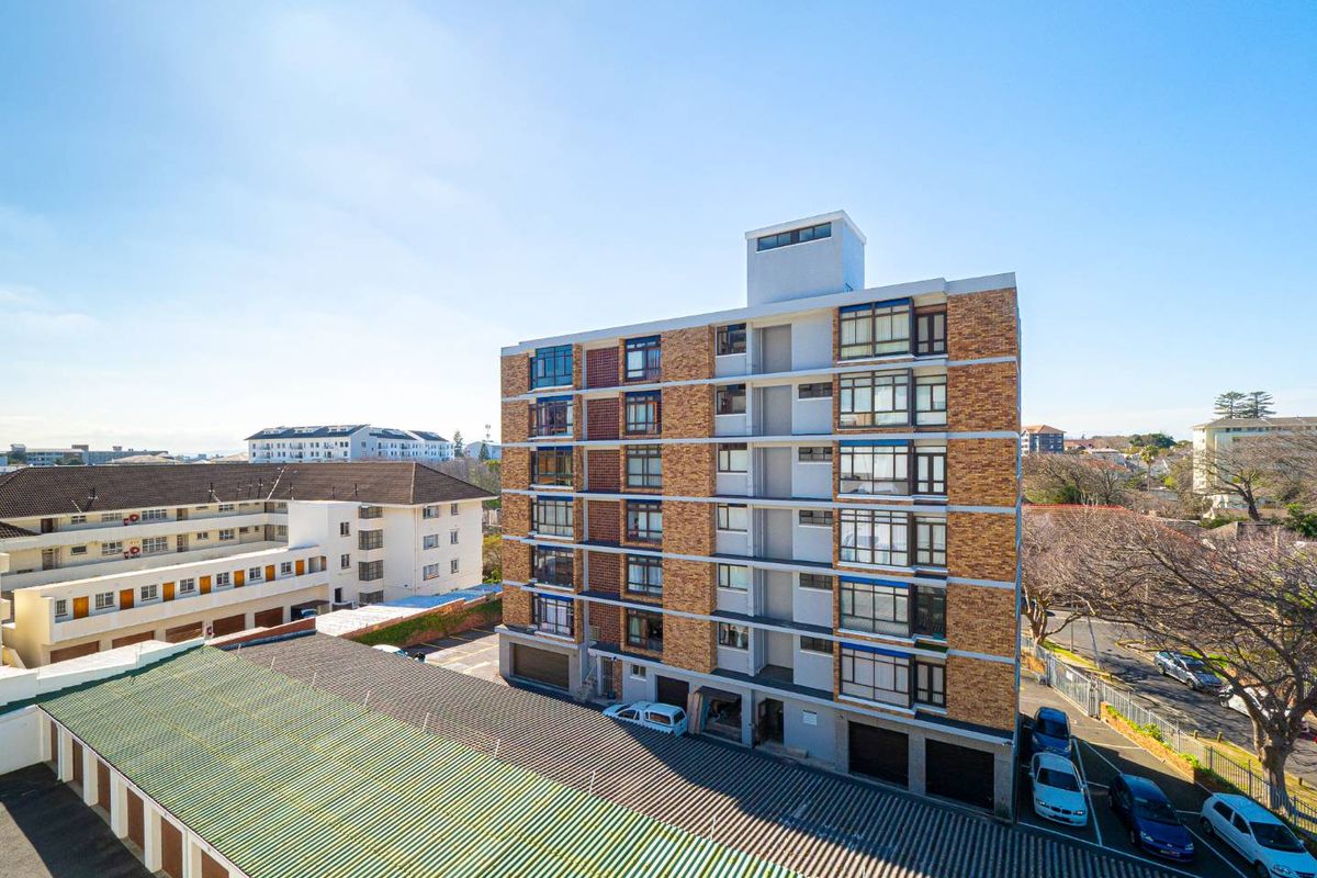 An elevated aerial view of a multi-story apartment building featuring brick and concrete facade construction with integrated window units and ground-level parking.