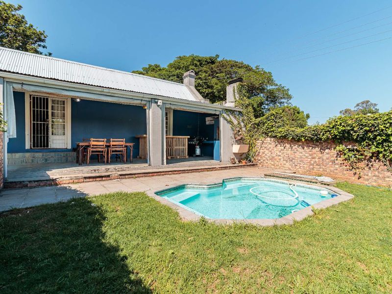 Outdoor entertainment area featuring a swimming pool, paved surround, and a covered patio with a built-in fireplace and brick boundary wall.