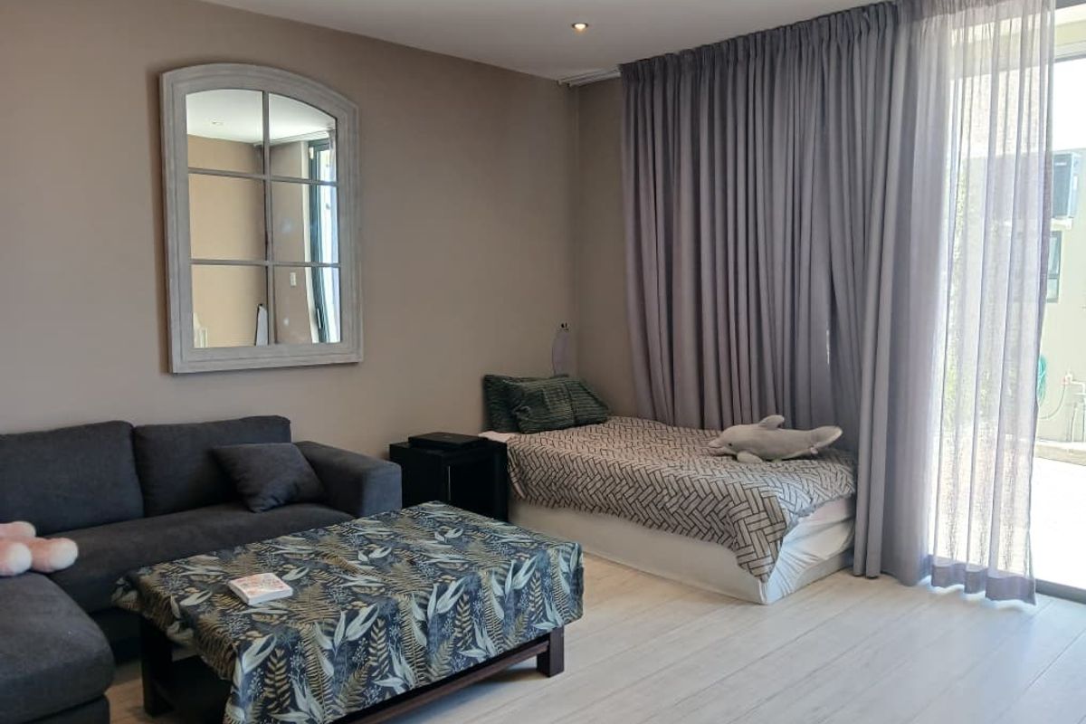 A well-maintained living area featuring light-toned flooring, recessed ceiling lighting, and large sliding glass doors with floor-to-ceiling curtains providing access to the exterior.