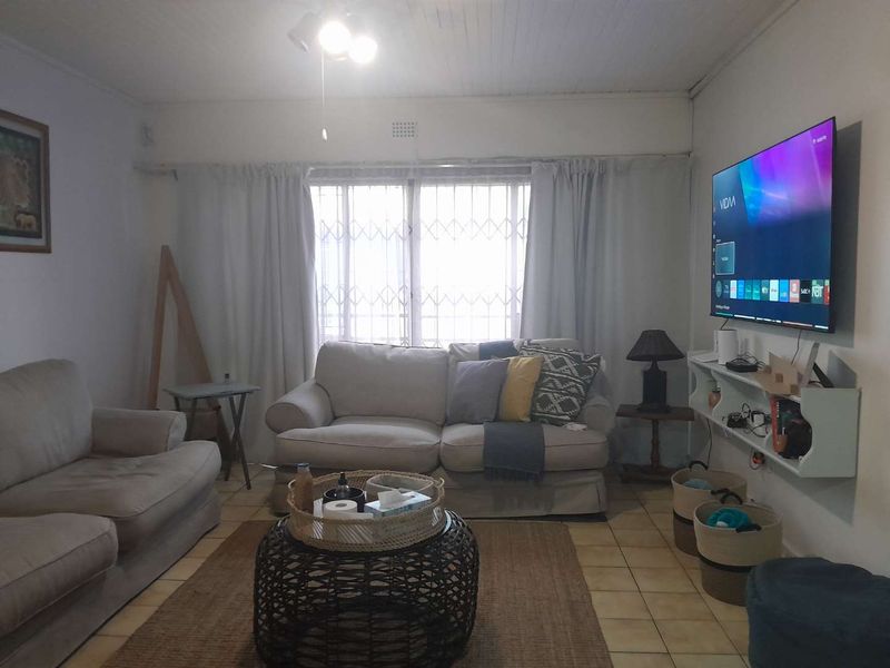 A comfortable living room featuring tiled flooring, a ceiling fan, and a security gate over the window, providing a functional and lived-in space.