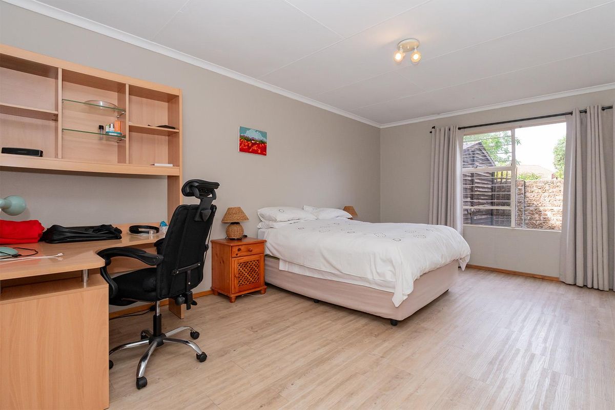 A spacious bedroom featuring light wood-look flooring, neutral wall tones, and a large window providing natural light.