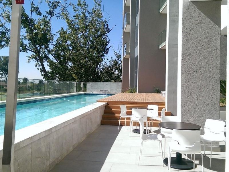 Modern outdoor pool area featuring a lap pool, glass balustrade, timber decking, and stone paved patio space.