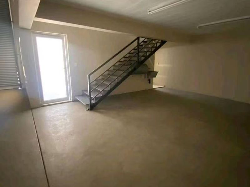 An open-plan garage space featuring concrete flooring, a metal staircase, and a built-in sink, offering a versatile area for storage or workshop use.