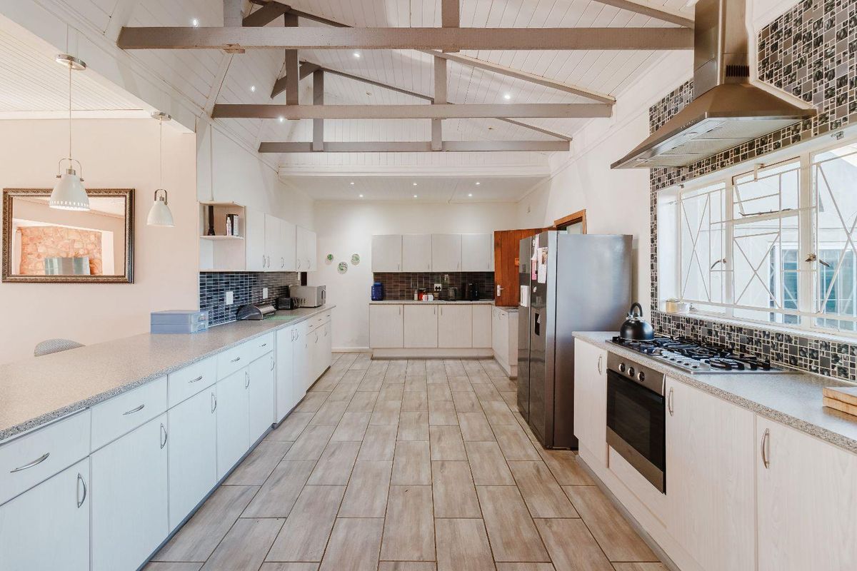 Spacious kitchen featuring vaulted ceilings with exposed beams, extensive built-in cabinetry, stone countertops, and integrated cooking appliances.
