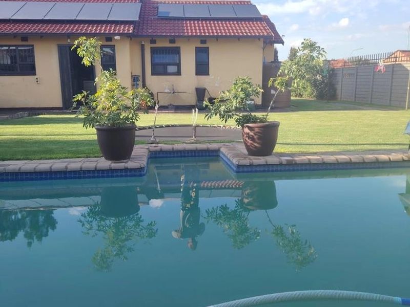 A backyard view featuring a swimming pool with brick coping, a lawn area, and a house exterior equipped with roof-mounted solar panels.