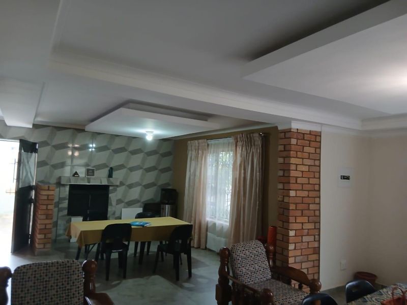 Open plan living area featuring a brick pillar, recessed ceiling detail, and a geometric tiled feature wall.