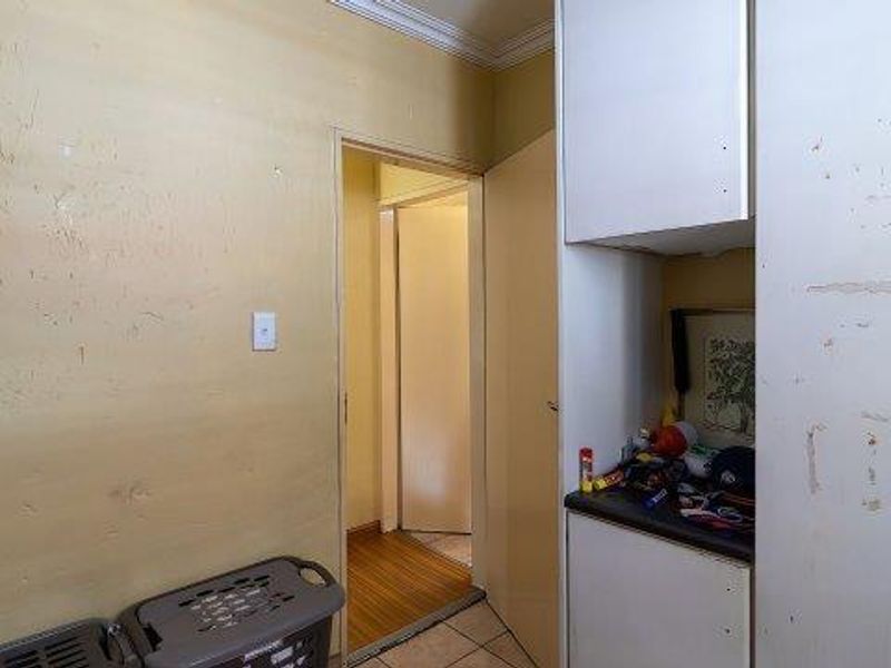A laundry area featuring built-in cabinetry and a mix of laminate and tiled flooring, currently showing significant wear and requiring cosmetic updates.