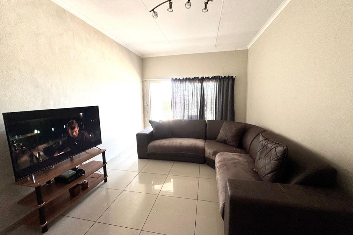 A living room featuring tiled flooring, a ceiling-mounted light fixture, and a sliding glass door providing natural light.