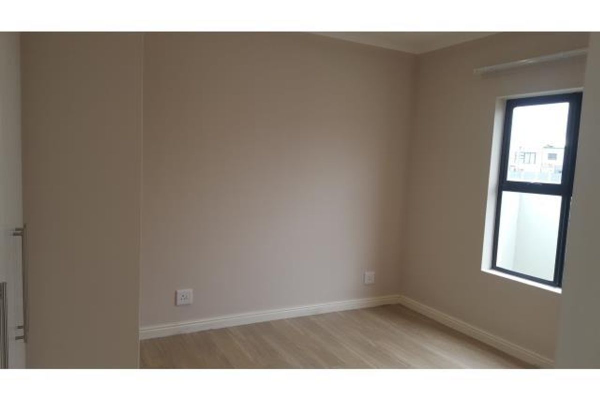 A clean, empty bedroom featuring neutral wall tones, modern laminate flooring, and a built-in cupboard with a sleek aluminium-framed window.