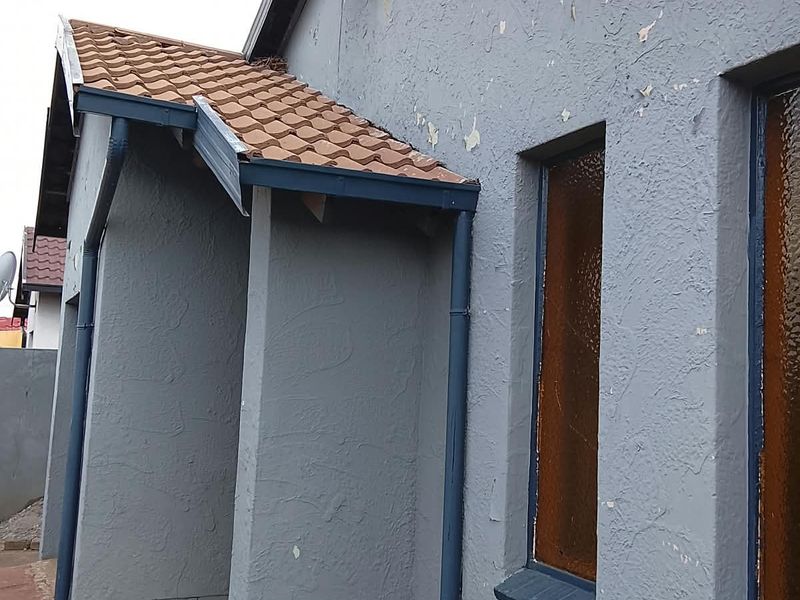Side view of the house exterior showing textured grey walls, tiled roof sections, and installed rainwater downpipes.