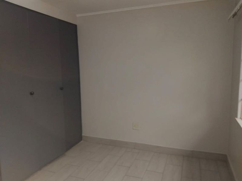 A clean, empty bedroom featuring modern grey built-in cupboards and neutral tiled flooring, providing a versatile space ready for personalization.